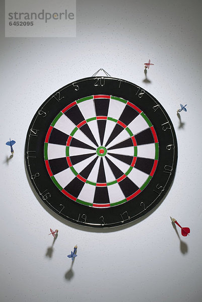 Darts in einer Wand rund um eine Dartscheibe geklebt