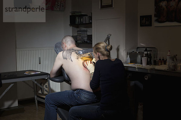 Eine Tätowiererin tätowiert den Rücken eines Mannes in einem Tattoo-Shop.