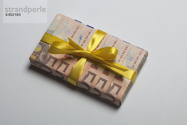 Fünfzig Euro-Banknoten  um ein Geschenk mit einer gelben Schleife zu verpacken.