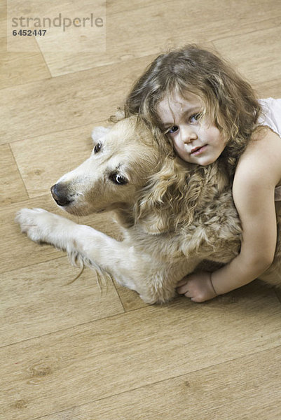 Ein junges Mädchen  das einen Hund umarmt.