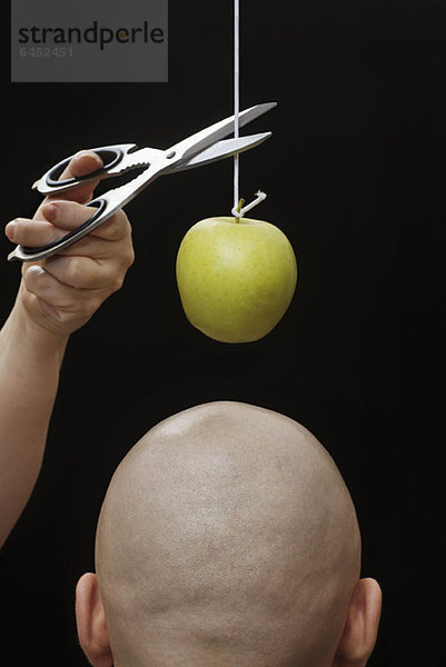Eine Frau schneidet einen Apfel an einer Schnur über dem Kopf eines Mannes.