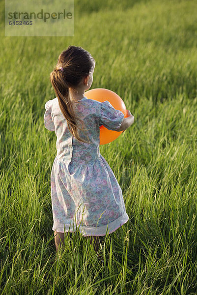 Rückansicht eines Mädchens  das einen Ballon auf einem Feld hält.