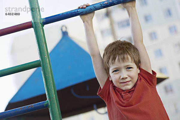 Ein Junge  der an einer Spielplatzbar hängt.