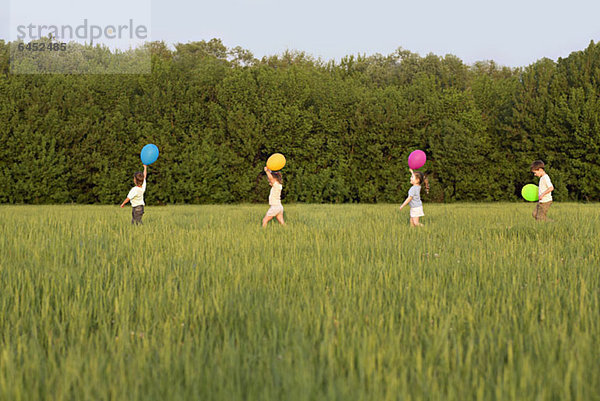 Kinder  die mit Luftballons auf einem Feld spazieren gehen.