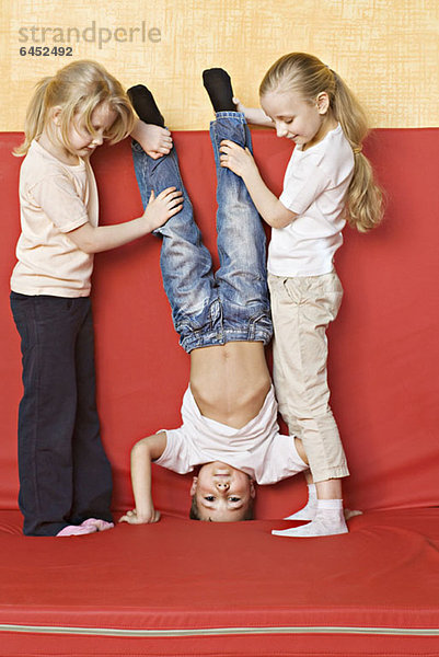 Zwei Mädchen halten einen Jungen auf dem Kopf.