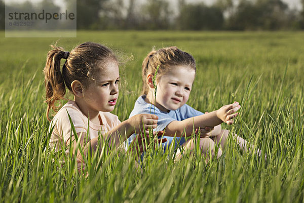 Zwei junge Mädchen  die auf einem Feld sitzen.