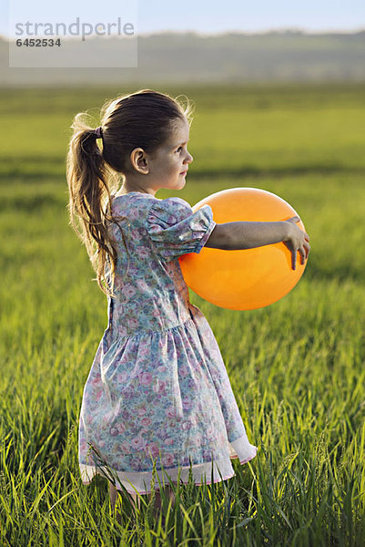 Seitenansicht eines Mädchens  das einen Ballon auf einem Feld hält.