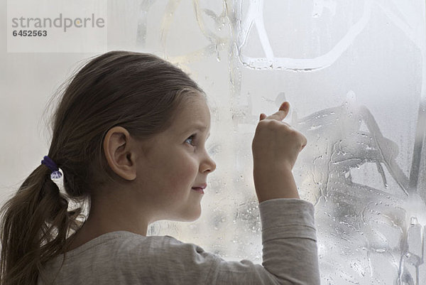 Ein Mädchen  das Kondensation auf Glas malt.