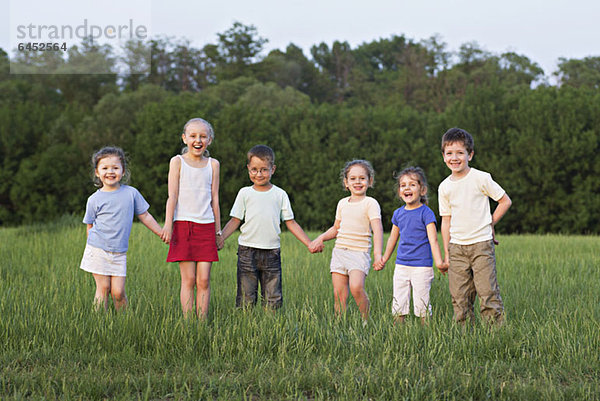 Kinder halten sich an den Händen und stehen auf einem Feld.