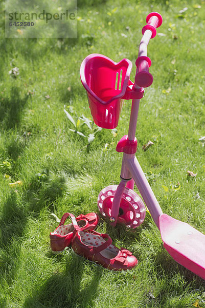 Ein rosa Schiebescooter und rosa Schuhe eines Kindes auf Gras