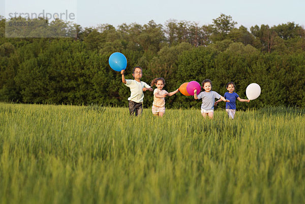 Kinder  die auf einem Feld mit Luftballons laufen