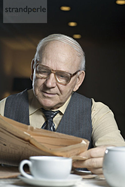 Ein älterer Mann  der eine Zeitung in einem Café liest.