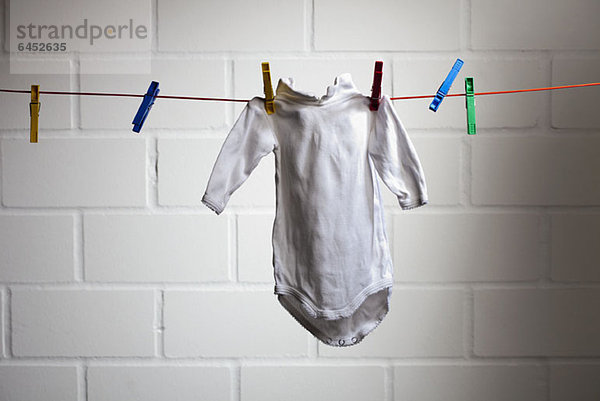 Der Strampler eines Babys hängt an einer Wäscheleine.