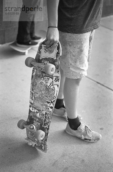 Ein Mann hält ein Skateboard  die Taille nach unten.