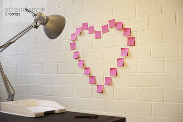 Herzförmig angeordnete Haftnotizen an einer Wand neben einem Schreibtisch
