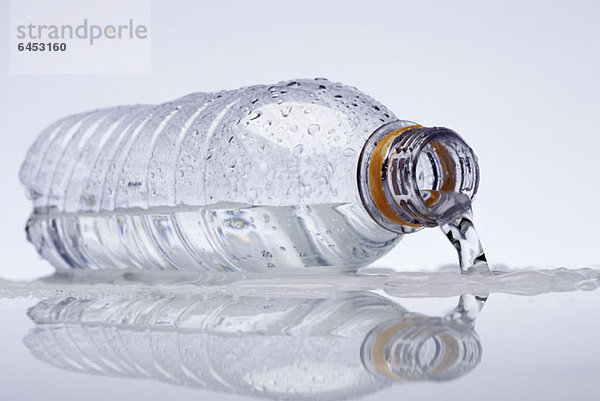 Eine Plastik-Wasserflasche  die auf der Seite liegt und Wasser ausläuft.