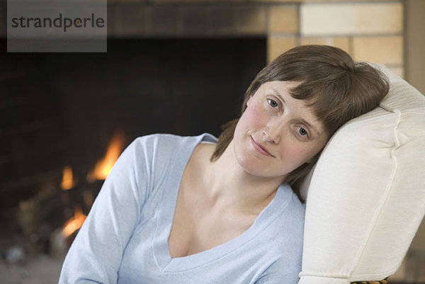 Eine heitere junge Frau sitzt in der Nähe eines brüllenden Feuers.