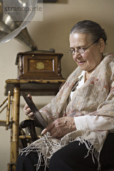 Eine ältere Frau  die intensiv auf eine Schallplatte schaut  Grammophon im Hintergrund