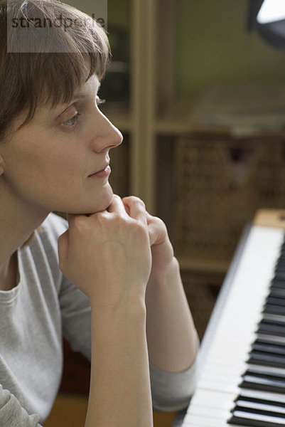 Eine Frau  die sich auf ein Klavier stützt und nachdenklich aussieht.