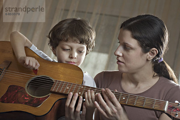 Eine Mutter hilft ihrem kleinen Sohn beim Spielen einer Akustikgitarre.