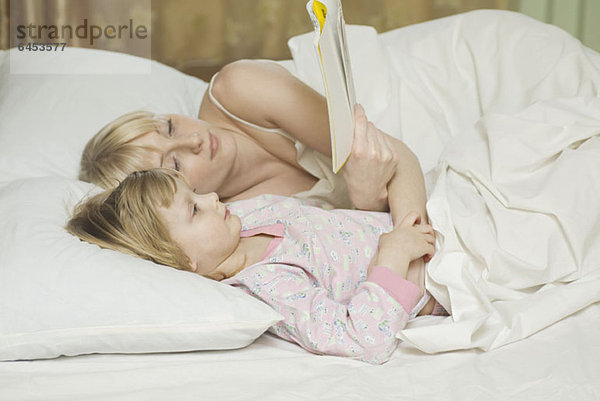 Eine Mutter und ihre kleine Tochter liegen im Bett und lesen ein Buch.