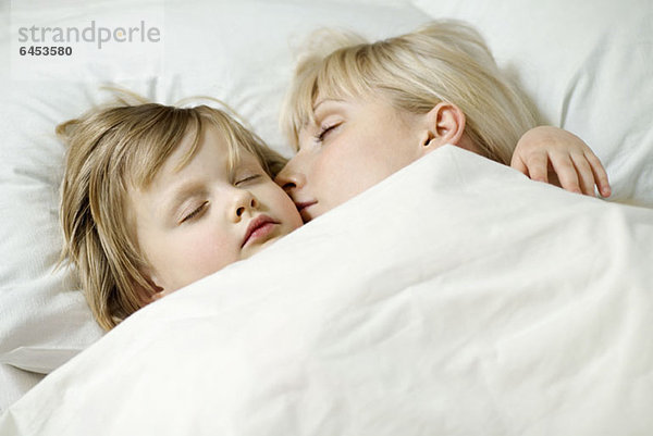 Eine Mutter und ihre kleine Tochter schlafen ein Bett nebeneinander.