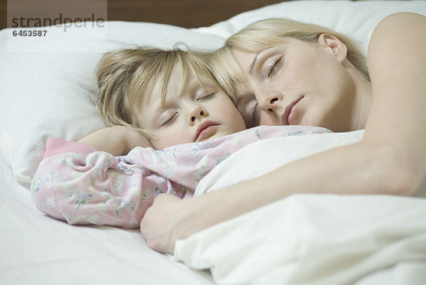 Eine Mutter und ihre kleine Tochter schlafen ein Bett nebeneinander.