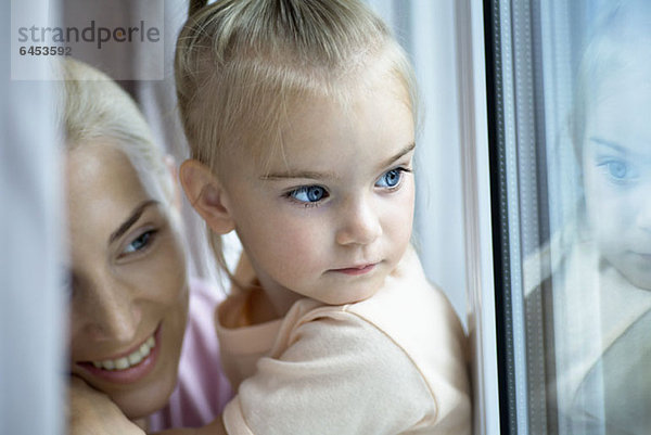 Eine Mutter und eine Tochter  die aus dem Fenster schauen.