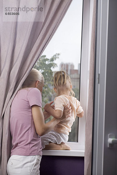 Eine Mutter und eine kleine Tochter  die aus ihrem Hausfenster schauen