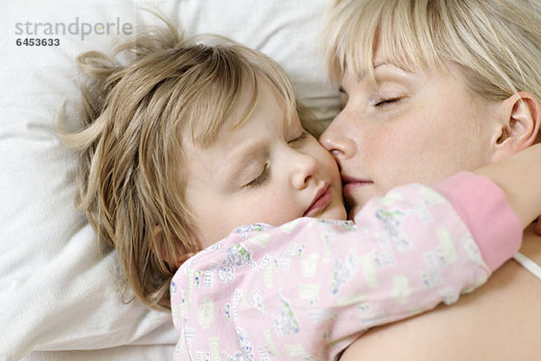 Eine Mutter und ihre kleine Tochter schlafen ein Bett nebeneinander.