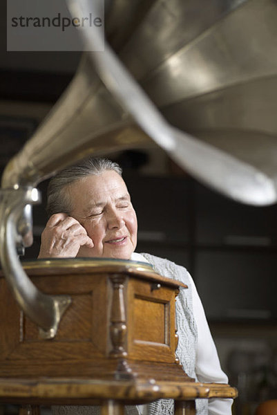 Eine Frau mit geschlossenen Augen  die einem Grammophon zuhört.
