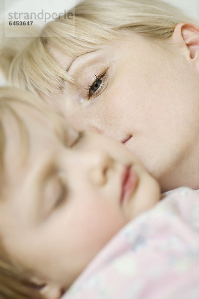 Eine Mutter  die neben ihrem schlafenden Kind aufwacht.