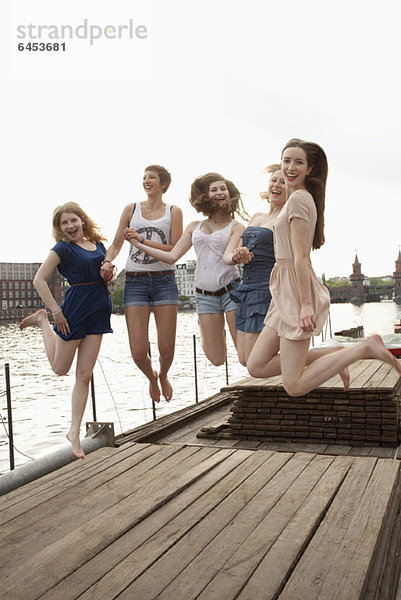 Fünf junge Freundinnen  die auf einem Steg an der Spree in die Luft springen.