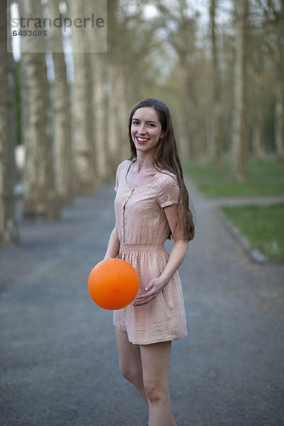 Eine junge Frau  die einen orangenen Ball hält und in einem Park steht.