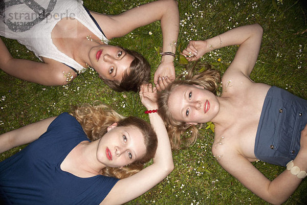 Drei Freundinnen liegen im Gras im Kreis und schauen sinnlich in die Kamera.