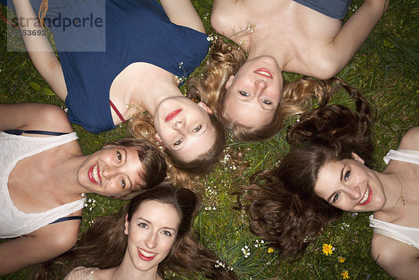 Fünf fröhliche Freundinnen liegen im Gras  Kopf und Schultern.