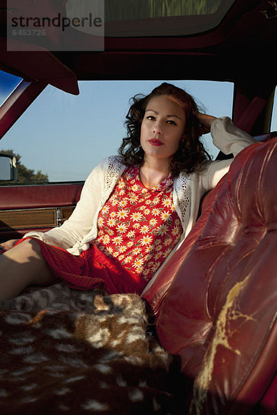 Eine hübsche Rockabilly-Frau sitzt auf dem Beifahrersitz eines Oldtimers.