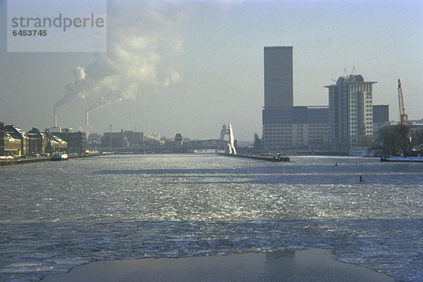 Blick über die Spree mit Industriekaminrauch und Statue des Molecule Man im Hintergrund