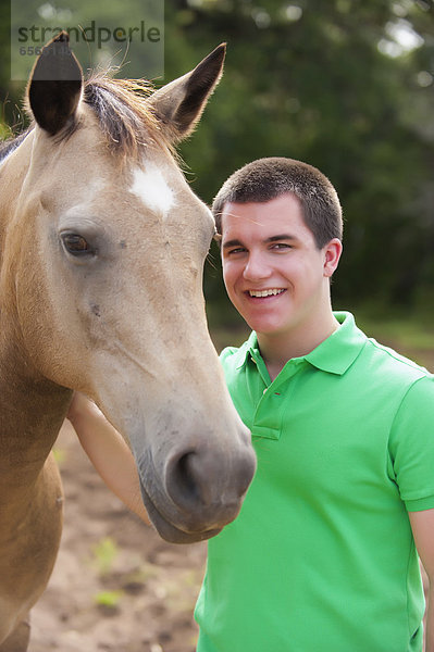 USA  Texas  Teenager Junge streichelndes Pferd  lächelnd  Portrait