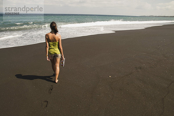 Indonesia  Young woman walking on black sand