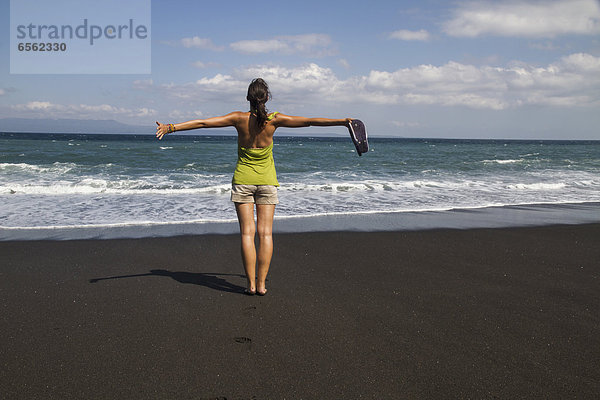 Indonesien. Junge Frau auf schwarzem Sand stehend