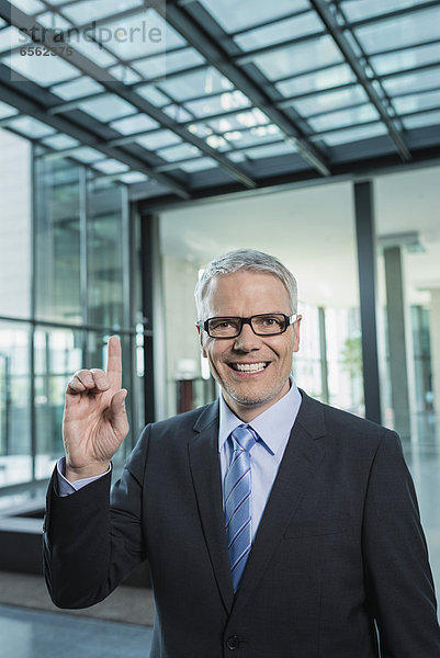 Deutschland  Stuttgart  Geschäftsmann mit einem Finger  lächelnd  Portrait
