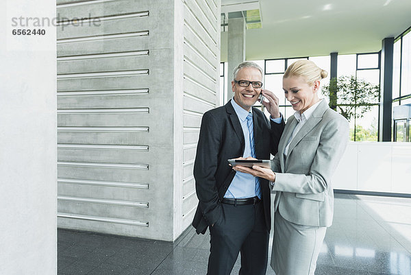 Businesswoman with digital tablet while man talking on phone