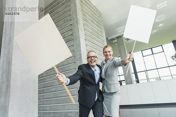 Germany  Stuttgart  Business people holding blank signs in office lobby  smiling  portrait