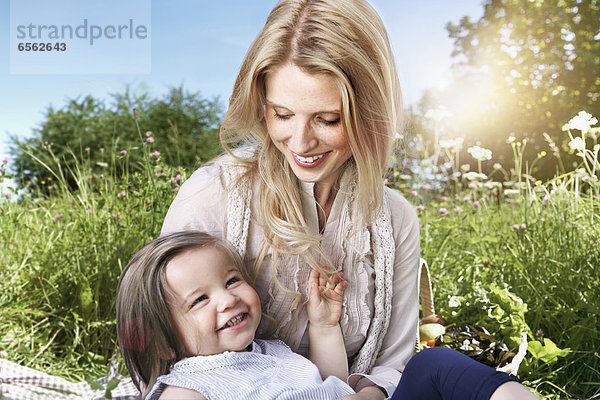 Germany  Cologne  Mother and daughter sitting on meadow  smiling