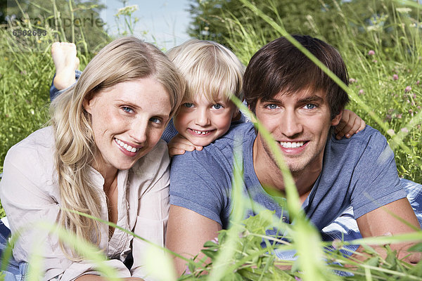 Germany  Cologne  Family lying in meadow  smiling  portrait