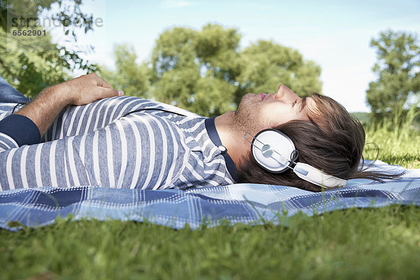 Junger Mann hört Musik auf der Wiese