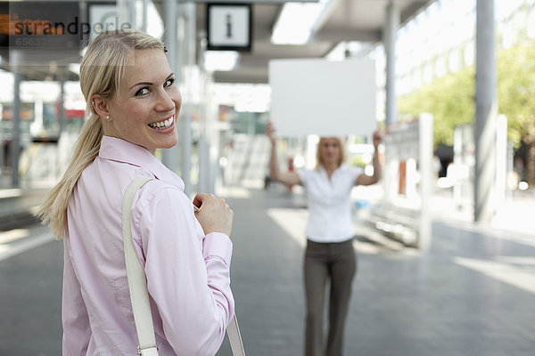 Junge Geschäftsfrau lächelnd  eine andere Frau mit Plakat im Hintergrund
