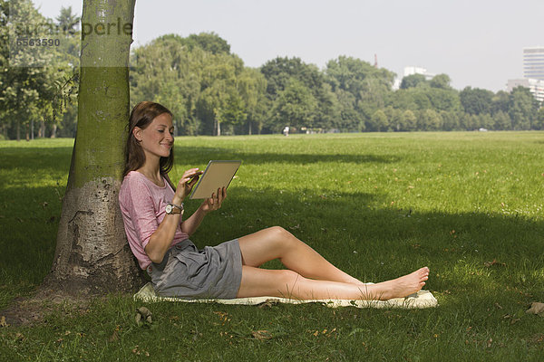 Germany  North Rhine Westphalia  Cologne  Young student sitting in park with digital tablet  smiling