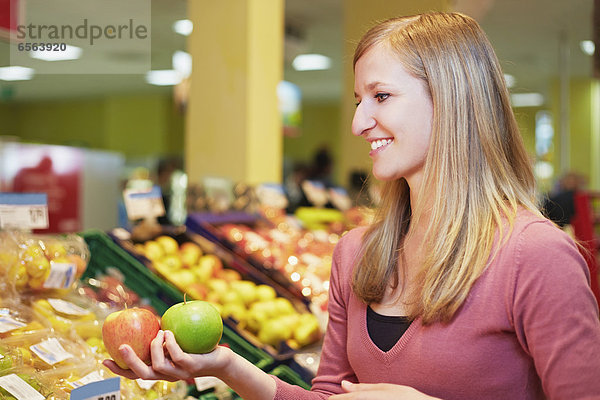 Young woman comparing apples in supermarket